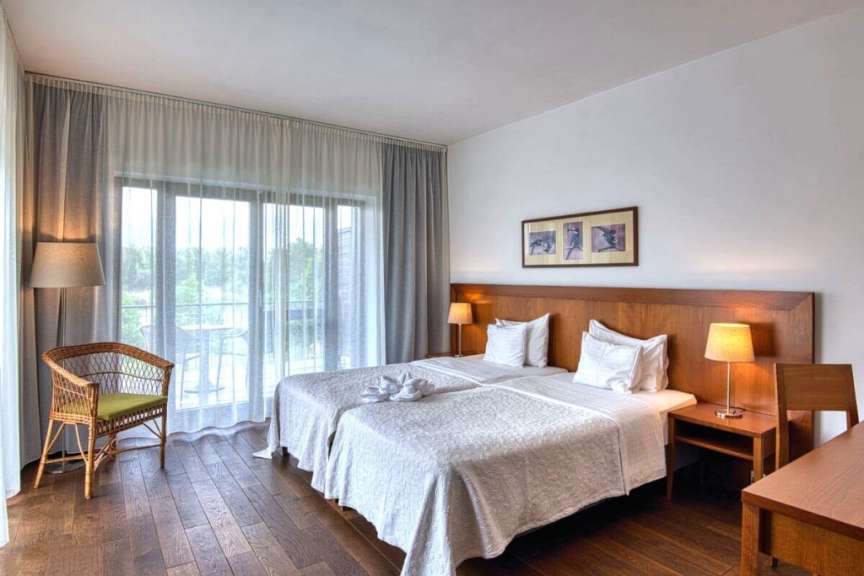 Ein geräumiges Hotelzimmer mit zwei Betten, einem Sessel und einer großen Balkontür.
