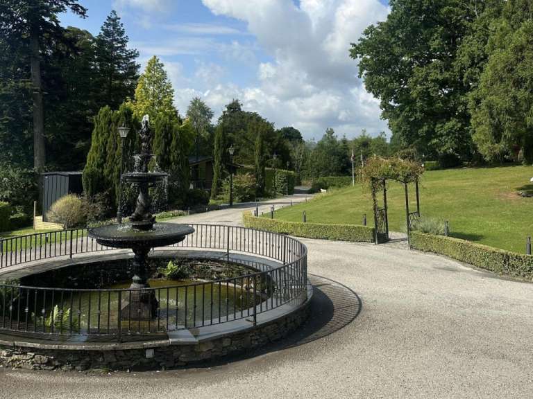 Ein Brunnen und eine Grünanlage mit einer Pergola sind in einem Park zu sehen.