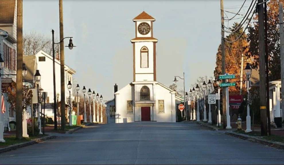 Eine Straße führt zu einer Kirche mit einem Glockenturm, die von Laternen und Häusern gesäumt ist.