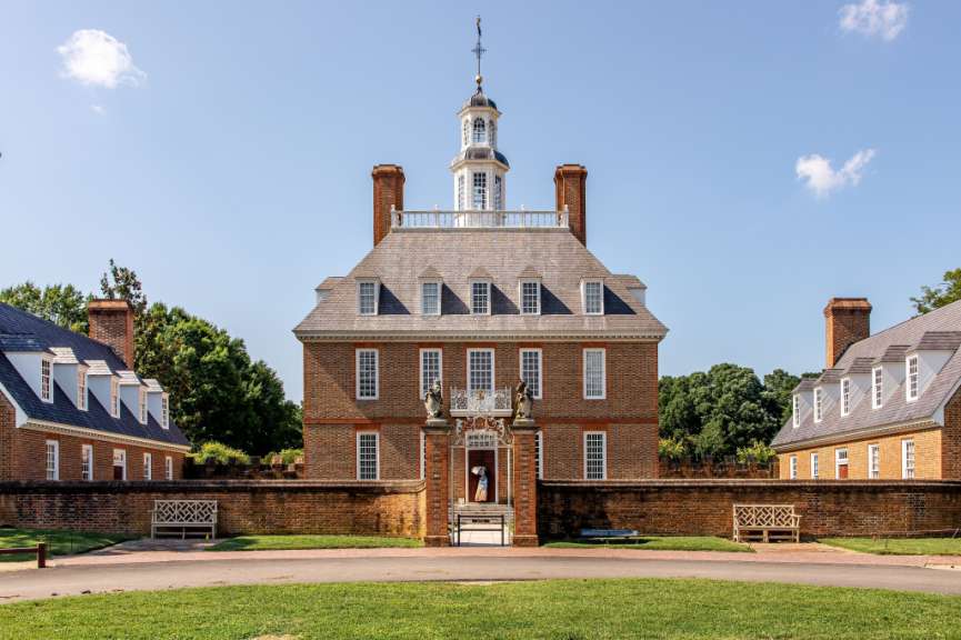 Die Governor's Palace von Williamsburg, Virginia, ist ein imposantes Backsteingebäude mit einem Kuppelturm und flankierenden Flügeln, umgeben von einer Ziegelmauer und gepflegten Grünflächen.