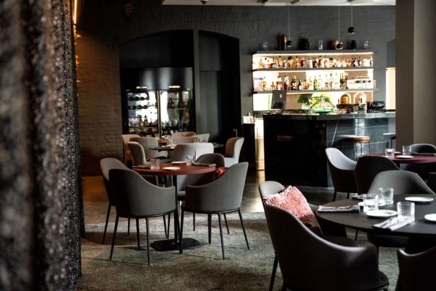 Ein gehobenes Restaurant mit dunkler Einrichtung und beleuchteten Regalen voller Flaschen ist auf dem Bild zu sehen.