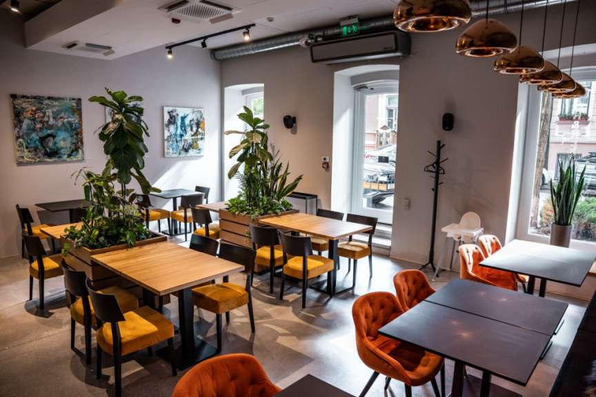 Das Bild zeigt den Innenraum eines Restaurants mit Tischen, Stühlen und Pflanzen.