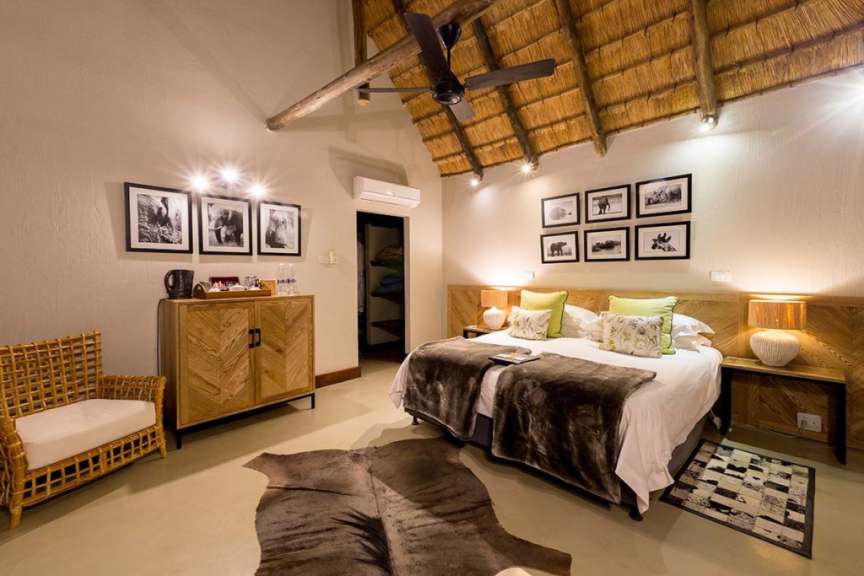 Ein Schlafzimmer mit zwei Betten, rustikalen Möbeln und afrikanischen Tierfotografien an der Wand.