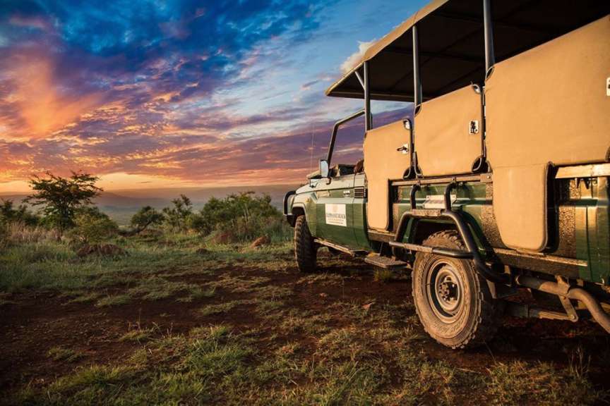 Ein Safari-Geländewagen steht auf einem Hügel vor einem dramatischen Sonnenuntergang.