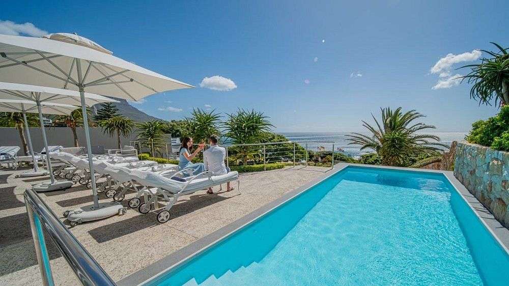 Ein Paar sitzt auf Liegestühlen am Pool und blickt auf das Meer.
