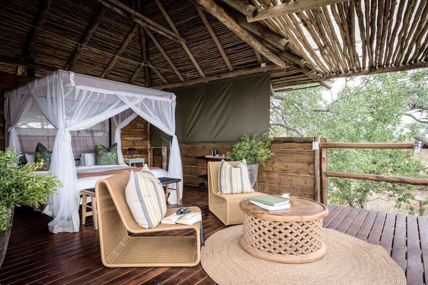 Auf einem hölzernen Deck befindet sich ein luxuriöses Zelt mit einem Himmelbett und Sitzgelegenheiten im Freien.