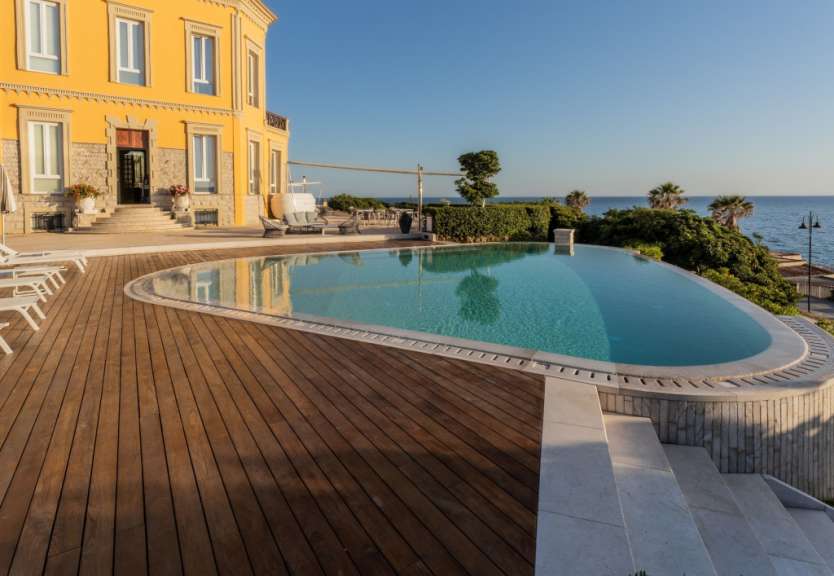 Ein gelbes Gebäude mit einem Infinity-Pool und Blick auf das Meer.