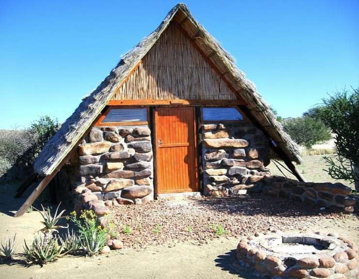 Ein kleines Steinhaus mit Strohdach und einem Lagerfeuerplatz davor.