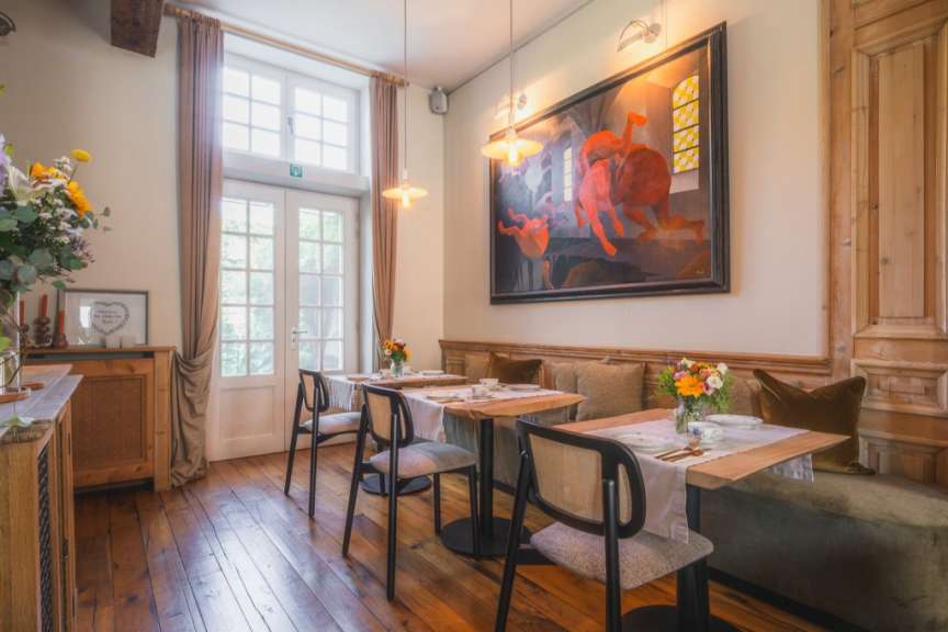 Der Speisesaal eines Hotels verfügt über Holztische und -stühle sowie einen großen Kunst-Druck über dem Essbereich.