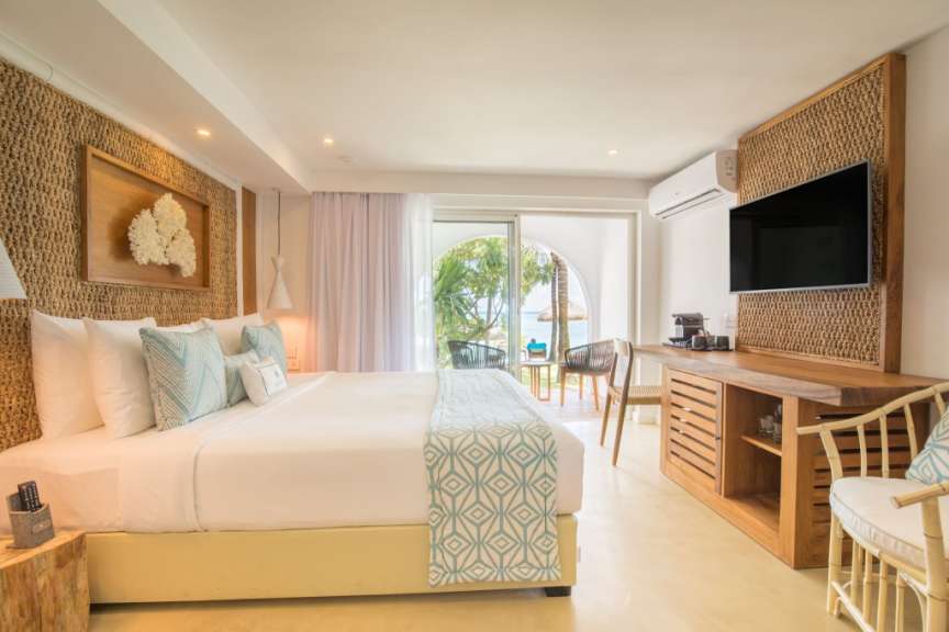 Ein gut beleuchtetes Hotelzimmer mit einem großen Bett, einem Fernseher und einem Blick auf das Meer.