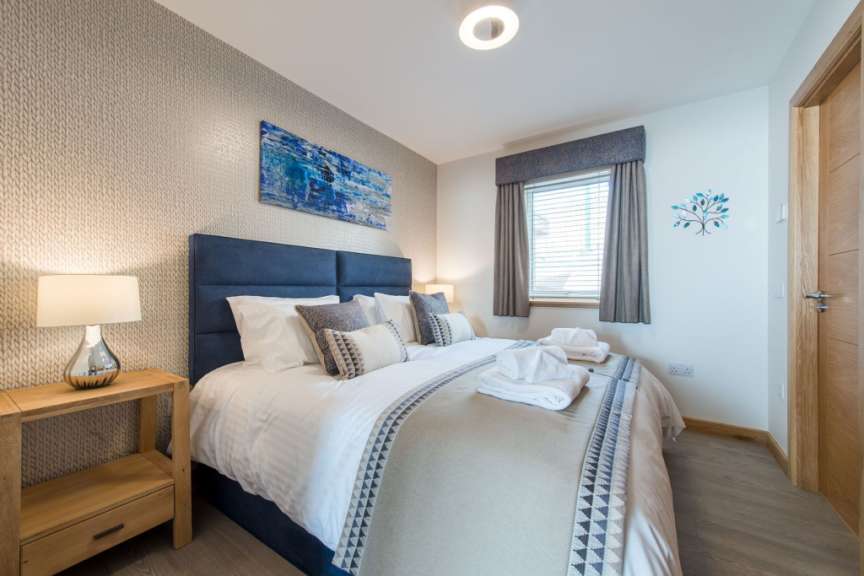 Ein Schlafzimmer mit einem großen Bett, einem Nachttisch mit Lampe, einem Fenster und einer Tür.