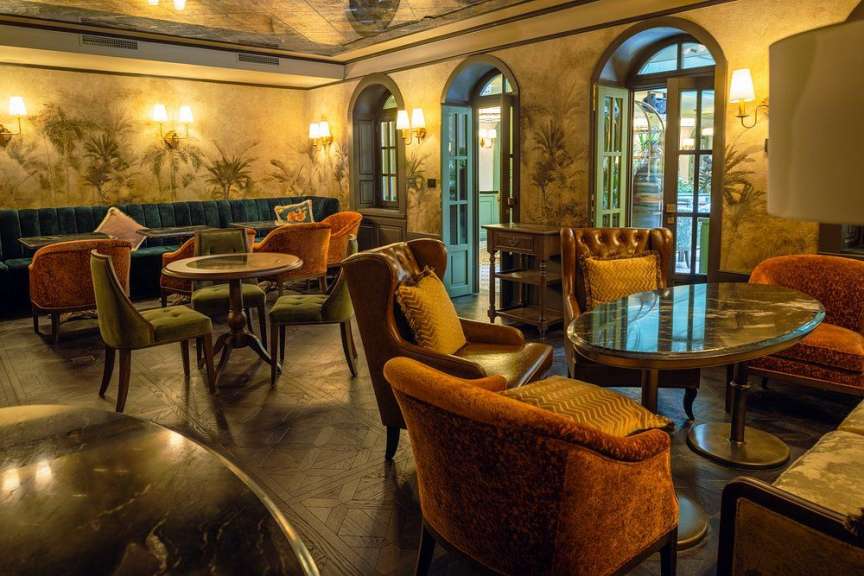In einem eleganten Raum stehen mehrere Sitzgruppen aus opulenten Sesseln und Sofas um Couchtische.