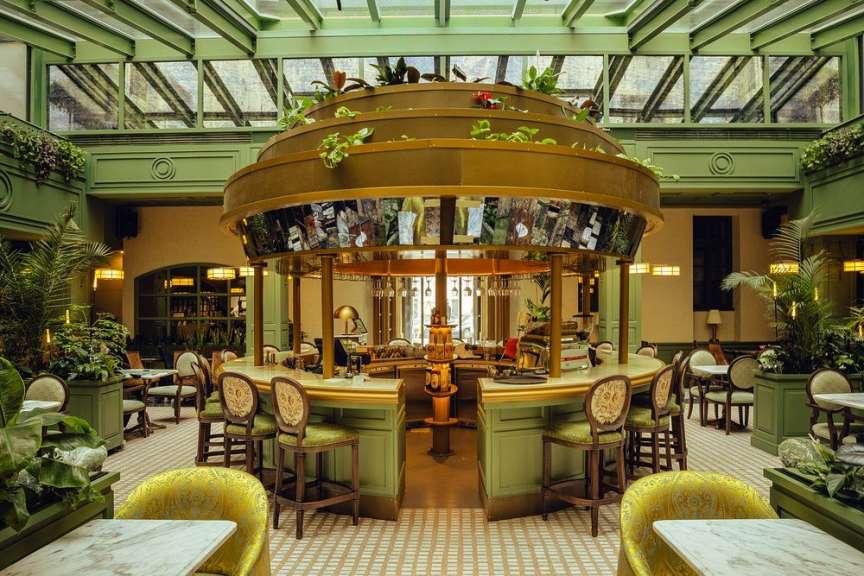 In diesem Bild ist ein stilvolles Interieur eines Restaurants mit einer runden Bar, grünen Akzenten und üppiger Vegetation zu sehen.