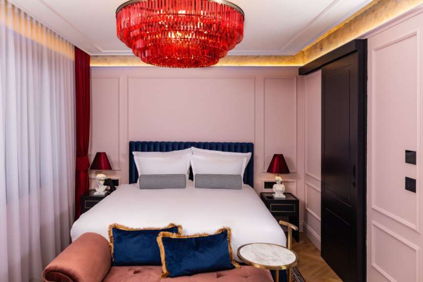 Ein luxuriöses Schlafzimmer mit einem Himmelbett, roten Samtvorhängen, einer opulenten roten Hängeleuchte und rosa Wandverkleidungen.