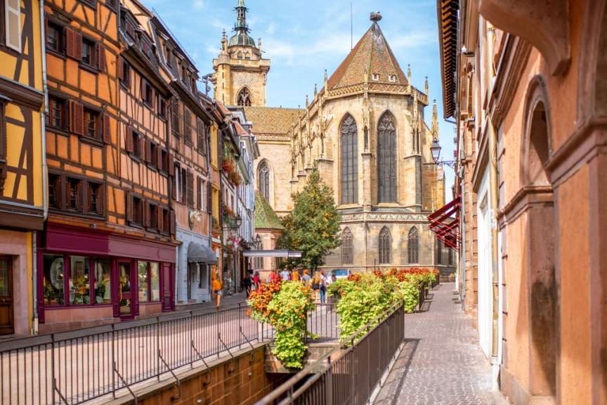 Eine Straße mit Fachwerkhäusern und einer Kirche im Hintergrund, gesäumt von Blumenkästen.