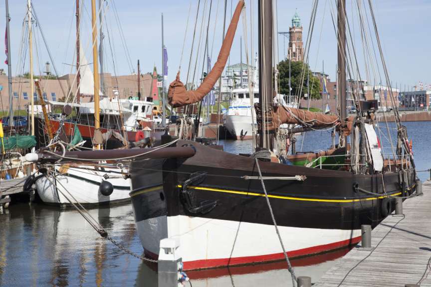 Auf diesem Bild sind mehrere Segelschiffe im Hafen zu sehen, mit einer markanten roten und weißen Silhouette auf dem Vordergrund.