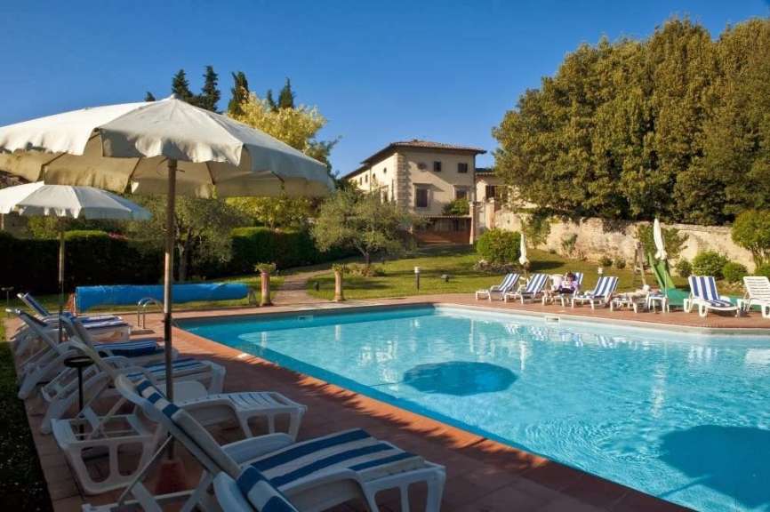 Ein großer Swimmingpool mit blauen Liegestühlen und Sonnenschirmen an einem sonnigen Tag mit einem Haus im Hintergrund.