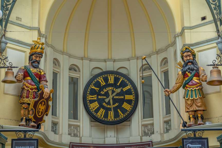 Zwei große, bemalte Figuren stehen auf beiden Seiten einer riesigen Uhr in einer Einkaufspassage.