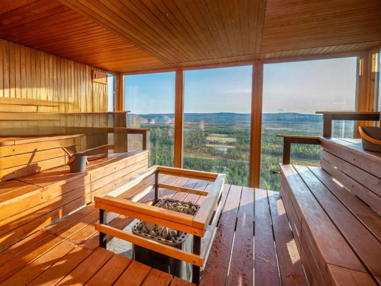 Eine hölzerne Sauna mit großen Fenstern bietet einen Panoramablick auf eine bewaldete Landschaft.