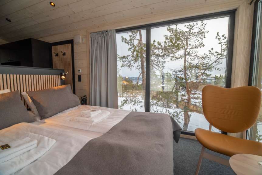 Ein gemütliches Schlafzimmer mit Doppelbett, Sitzgelegenheit und großem Fenster, das auf eine verschneite Waldlandschaft blickt.