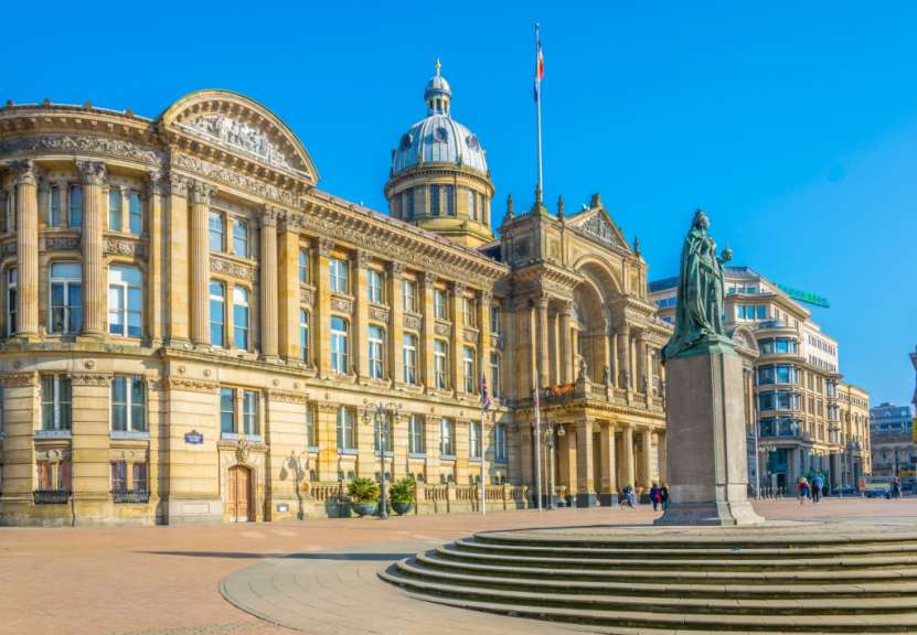 Auf diesem Bild ist die Statue von Queen Victoria auf dem Victoria Square in Birmingham vor dem Rathaus und einer modernen Glasfassade zu sehen.
