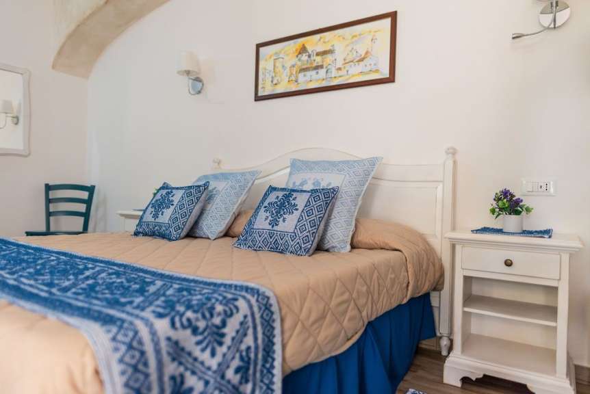 Das Bild zeigt ein Schlafzimmer mit einem Bett, das mit blau-weißen Kissen und einer Tagesdecke dekoriert ist.