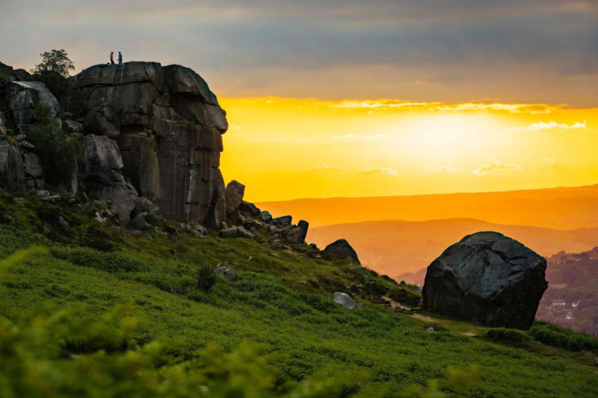 Zwei Personen stehen auf einem Felsen vor einer atemberaubenden Landschaft im Abendlicht.