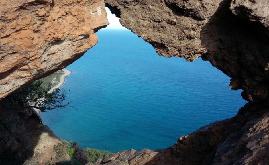 Durch eine Felsöffnung blickt man auf das tiefblaue Meer und eine Küstenlinie.