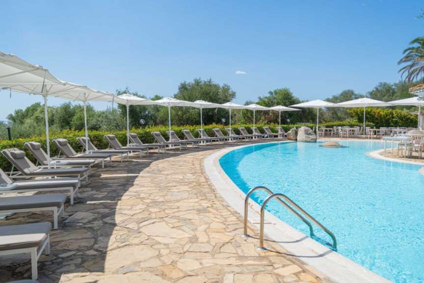 Ein Swimmingpool mit Sonnenliegen und Sonnenschirmen, umgeben von einem Steingarten und Bäumen.