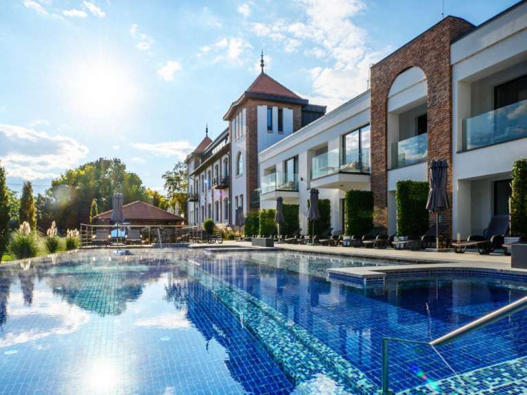 Ein modernes Hotel mit einem Schwimmbecken und Liegestühlen vor einem sonnigen Himmel.