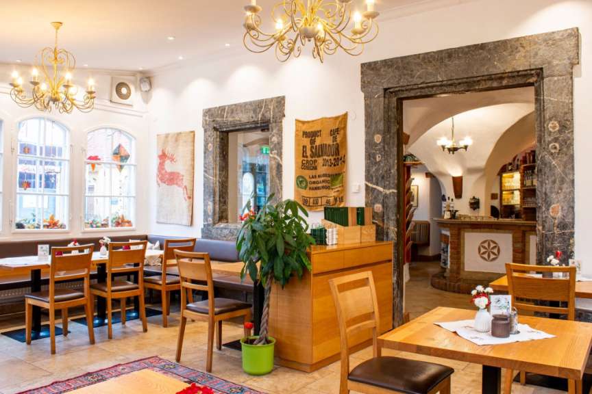 Dieses Bild zeigt das Innere eines Restaurants mit Holztischen, Stühlen und dekorativen Wandbehängen.