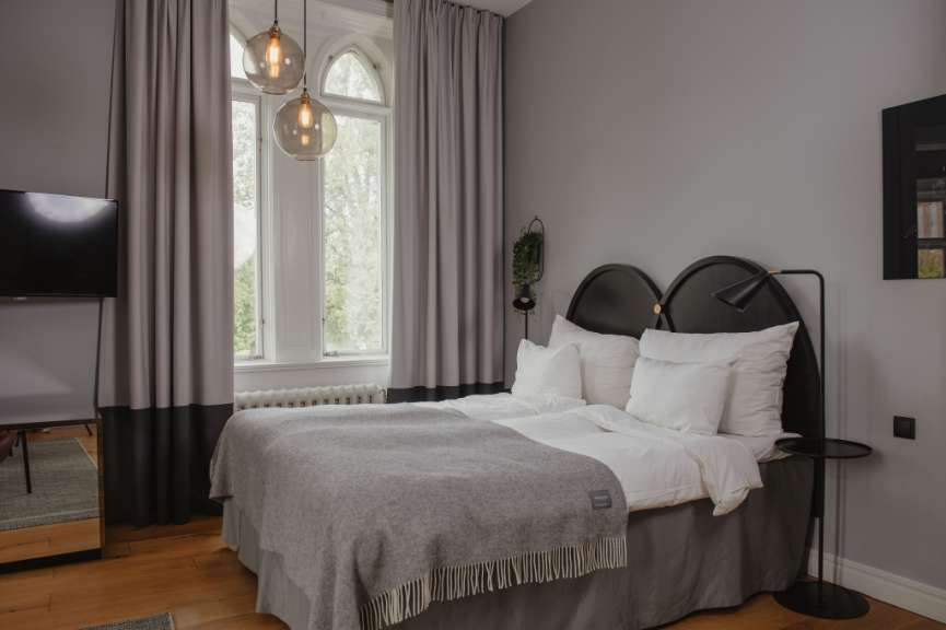 Ein Schlafzimmer mit einem Bett, Fernseher, Vorhängen, einem Fenster und einem Gemälde.