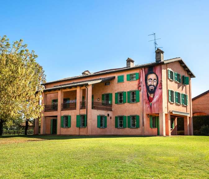 Ein großes, rosafarbenes Gebäude mit grünen Fensterläden wird von einem riesigen Wandgemälde des Opernsängers Luciano Pavarotti geschmückt.