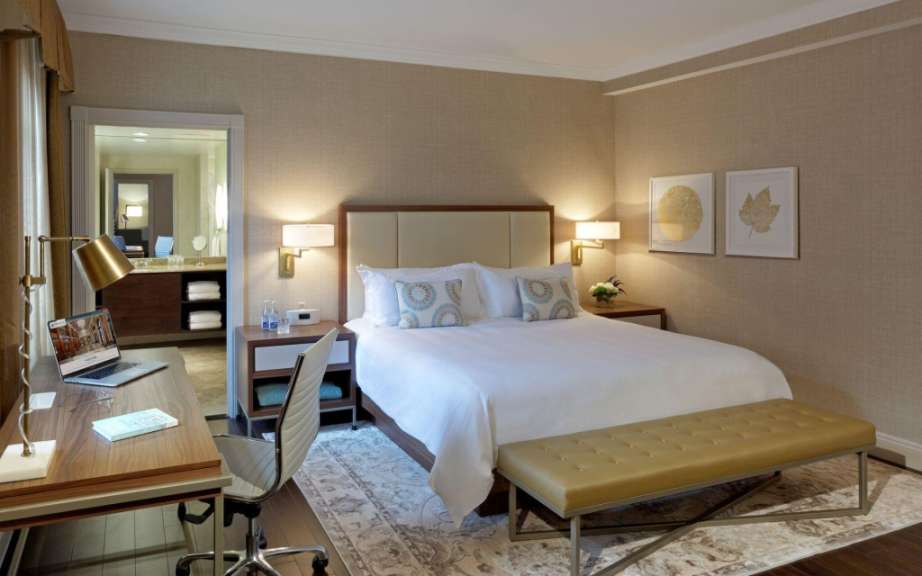 Ein Schlafzimmer mit einem Bett, einem Schreibtisch und einem Eingang zu einem Badezimmer wird gezeigt.