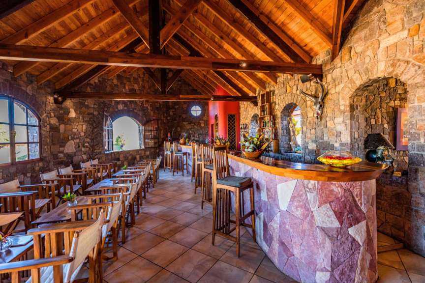 Ein Restaurant mit Holzdach, Steinfassade und Holztischen und -stühlen ist zu sehen.