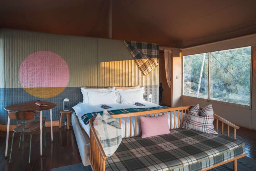 Ein luxuriöses Schlafzimmer mit einem Bett, einem Sofa, einem runden Tisch und einem großen Fenster mit Blick auf die Natur.