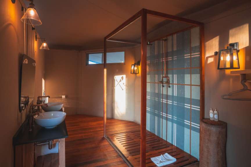 Die warme Beleuchtung und das Holz schaffen eine luxuriöse Atmosphäre in diesem Badezimmer mit Doppelwaschbecken und einer Duschkabine.