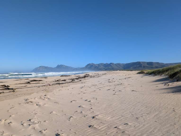 Ein weites Bild eines leeren Strandes mit Sanddünen und Bergen im Hintergrund.