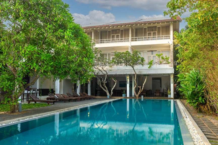 Ein Hotel mit Swimmingpool und umgebenden Bäumen unter einem bewölkten Himmel.