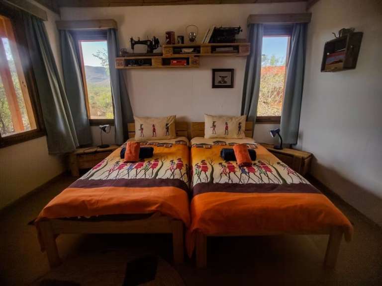 Ein Schlafzimmer mit zwei Betten, die mit bunten Bettdecken und Kissen mit afrikanischen Motiven dekoriert sind.