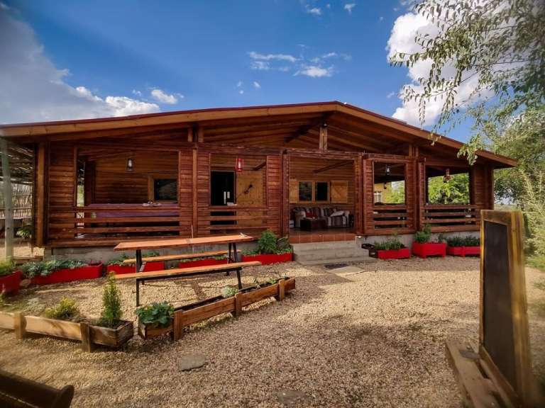 Ein rustikales Holzhaus mit einer Veranda, vor dem Kies und Blumenkästen stehen.
