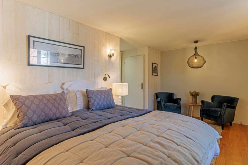 Ein Schlafzimmer mit einem großen Bett, zwei Sesseln und einem Nachttisch ist zu sehen.