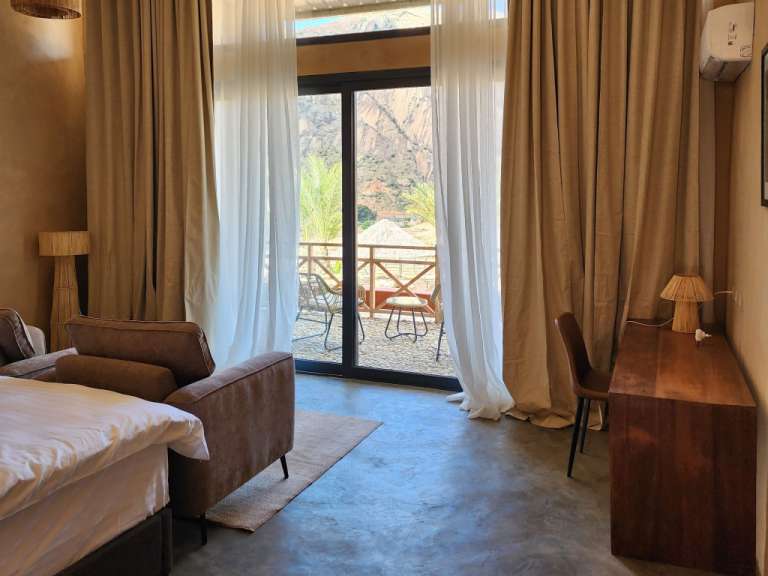 Ein Schlafzimmer mit Balkontür und Bergblick, das von braunen und weißen Vorhängen eingerahmt wird.