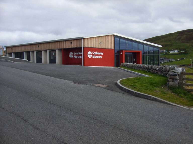 Ein modernes Museum mit roten und holzverkleideten Fassaden steht an einem bewölkten Tag vor einer grünen Hügellandschaft.