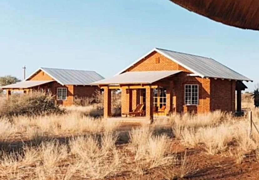Auf dem Bild sind zwei kleine Backsteinbungalows mit Metallschrägdächern in einer trockenen Graslandschaft zu sehen, die an einem sonnigen Tag von der Seite aufgenommen wurden.