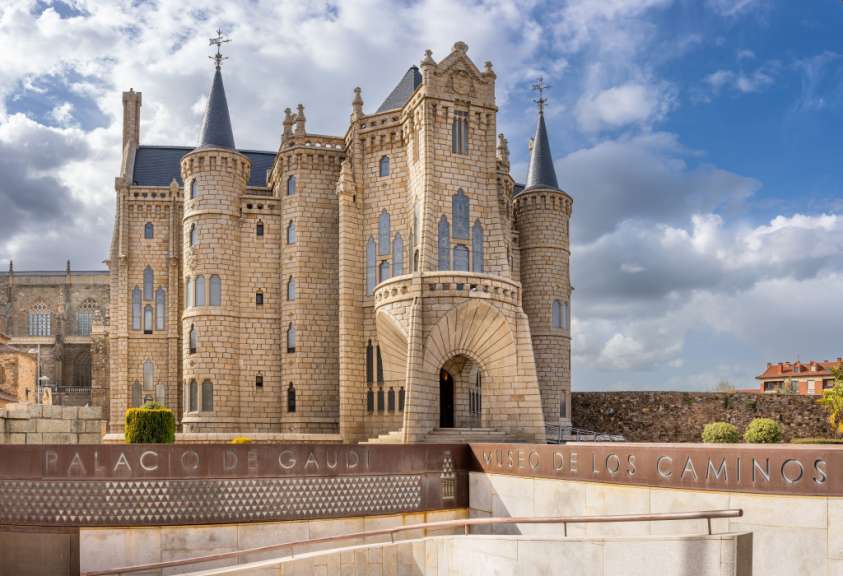 Das Bild zeigt den Palacio Episcopal in Astorga, ein Werk von Antoni Gaudí, mit einer Beschilderung, die auf „Palacio de Gaudí“ und „Museo de los Caminos“ hinweist.
