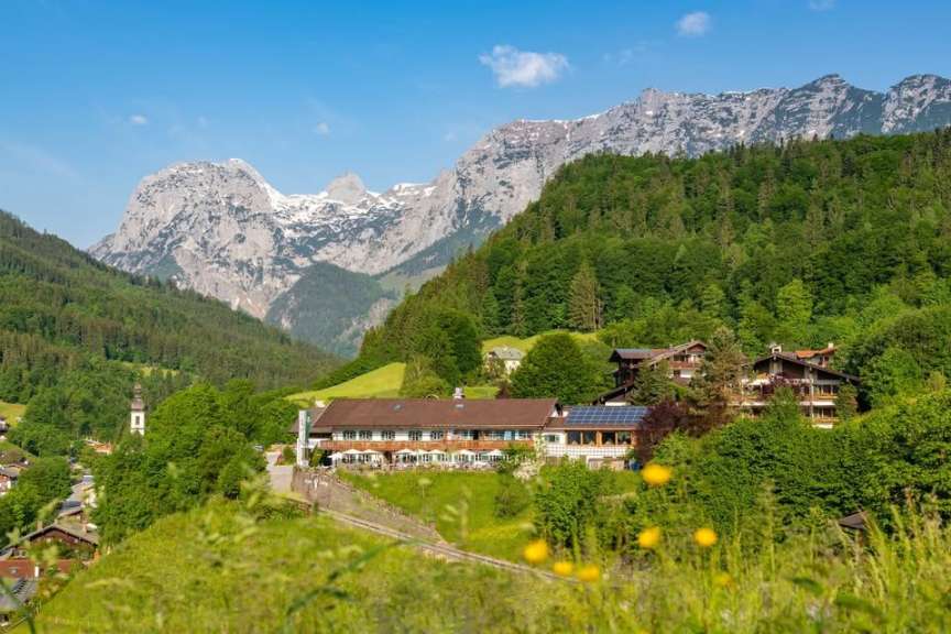 Ein Hotel mit Solarzellen und Solarpaneelen steht in einem grünen Tal vor einer Bergkulisse.