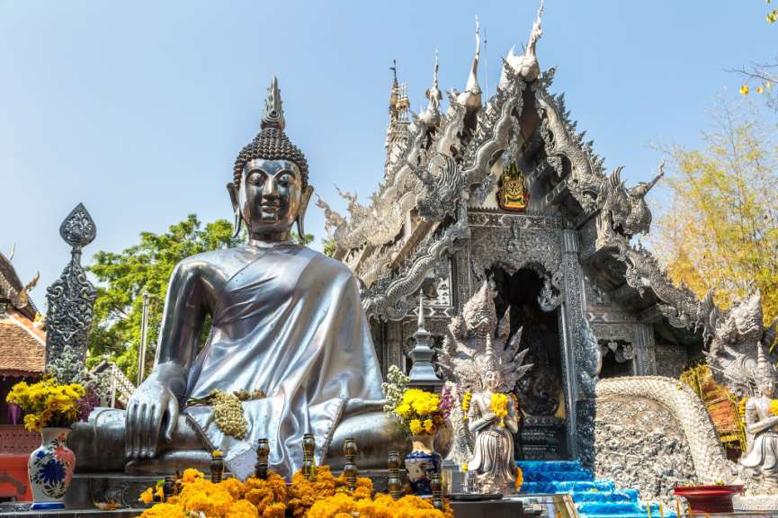 Ein großer, silberner Buddha sitzt vor einem kunstvoll verzierten, silbernen Gebäude mit aufwendigen Drachenfiguren.