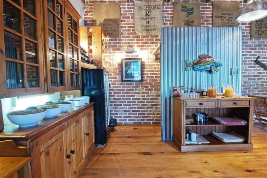 Ein Selbstbedienungsbuffet mit Speisen und Getränken, geschmückt mit Kaffeetüten und einer bunten Fischdekoration, steht vor einer Ziegelwand.