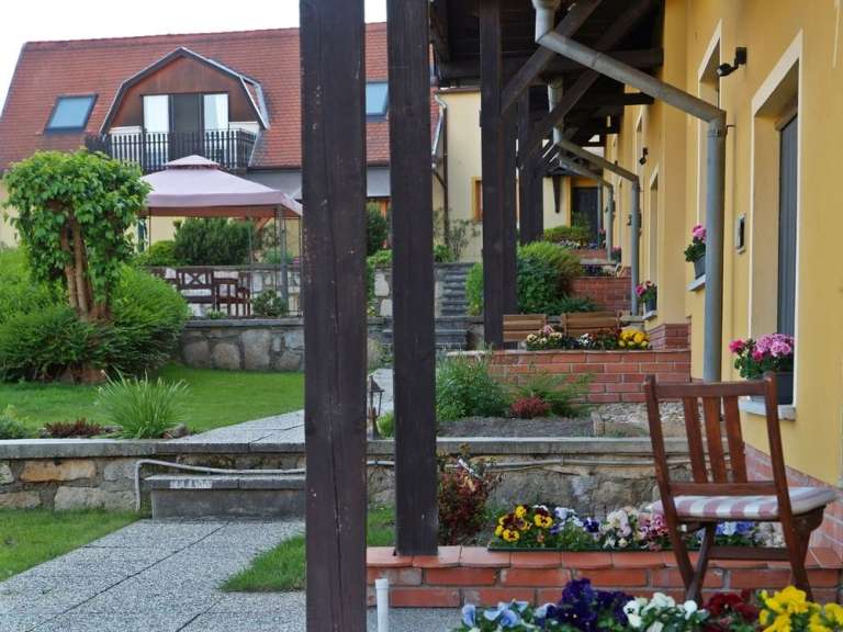 Ein Holzsessel steht vor einer gelben Hauswand mit einer Reihe von kleinen Blumentreppen auf der rechten Seite des Bildes.